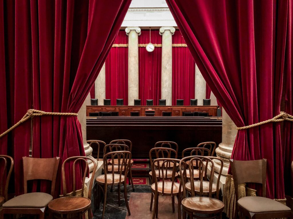 The interior of the Supreme Court's courtroom, showing the empty chairs where the nine justices sit and many empty chairs and benches in the visitors' seating area.